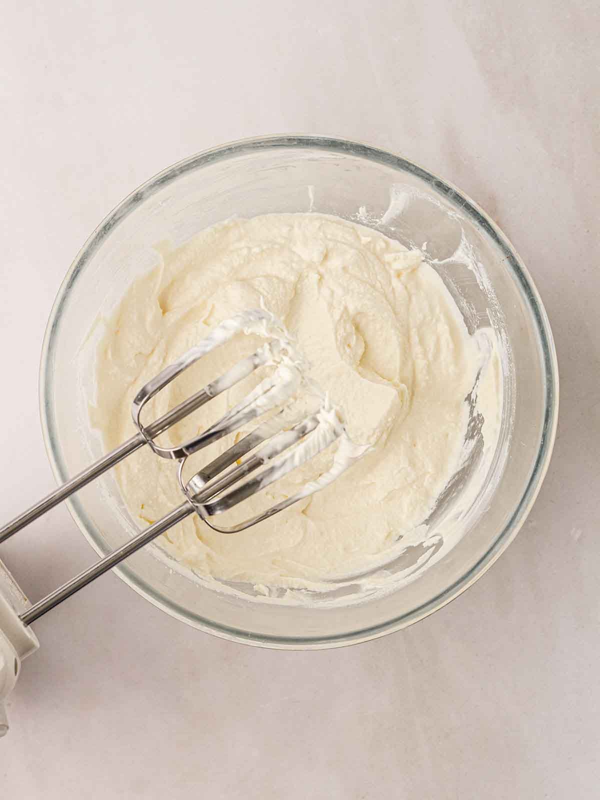A glass bowl with whipped cream with a whisk in.