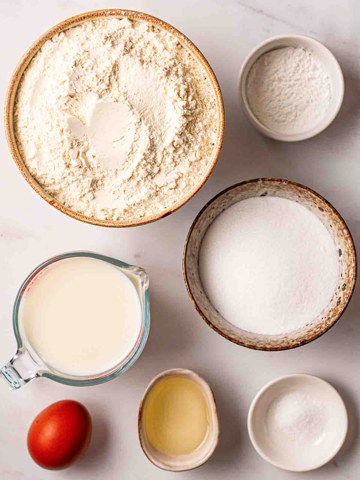 The ingredients for American Pancakes laid out on a counter top. A view from above, with the ingredients in separate bowls.