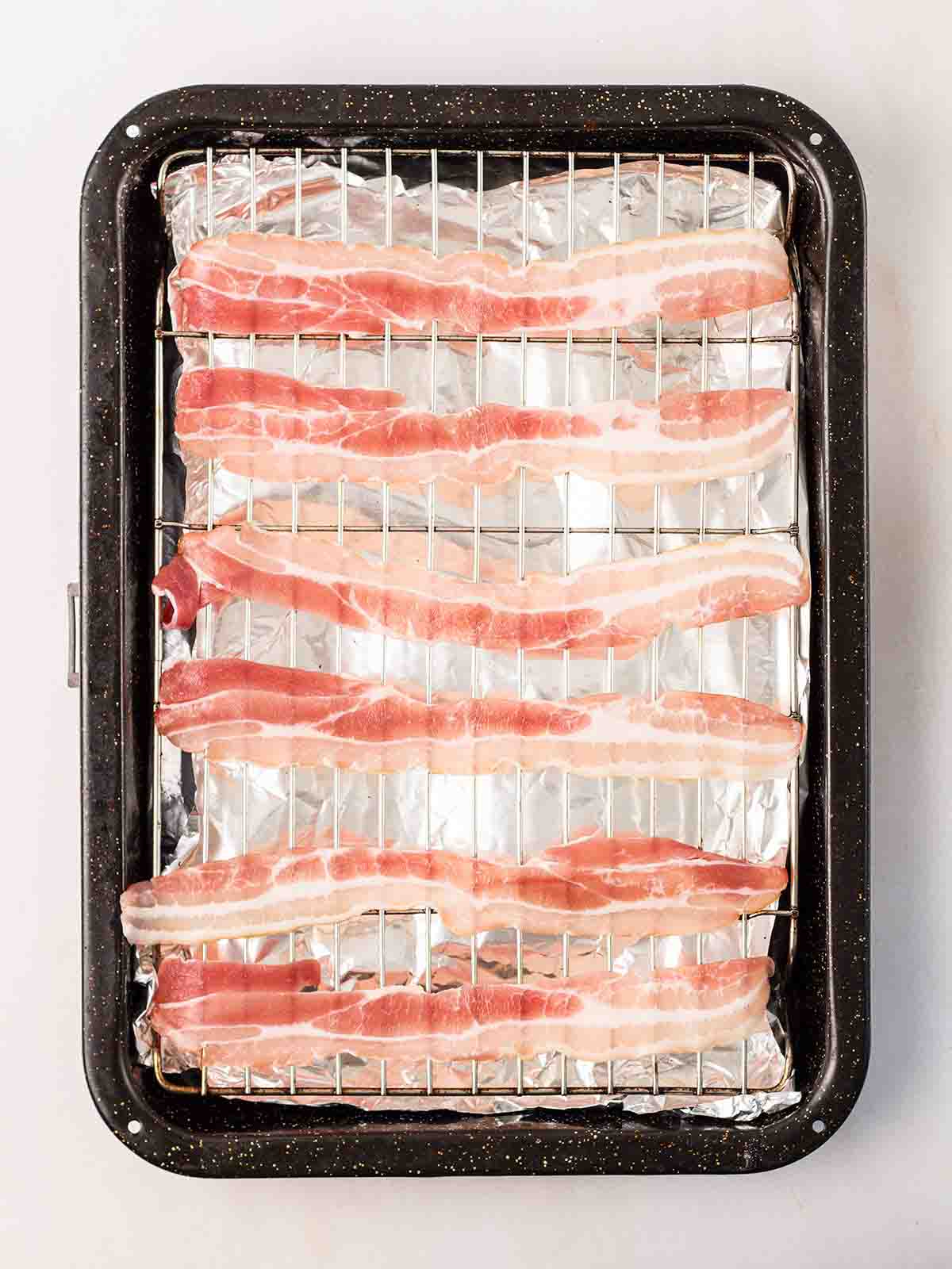Raw streaky bacon on a grill pan with foil underneath.