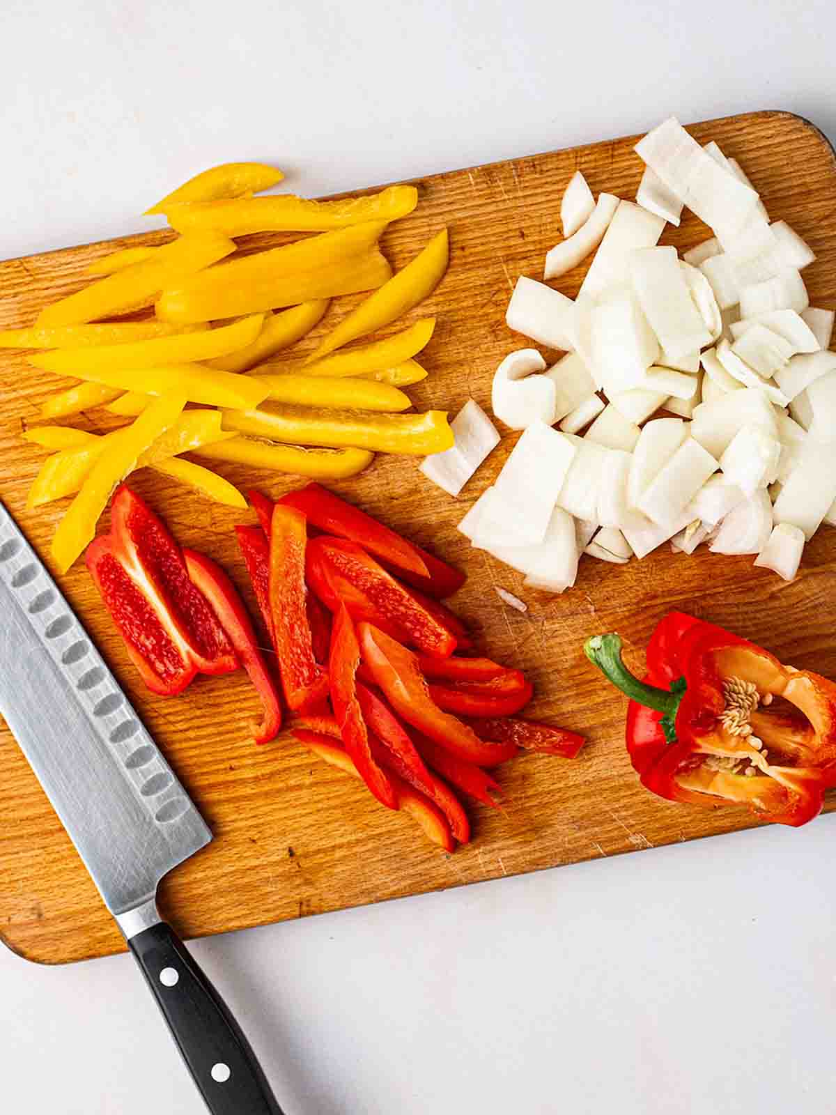 Peppers and onions sliced on a chopping board with a knife to the side for step 1 in the recipe for Halloumi Fajitas.