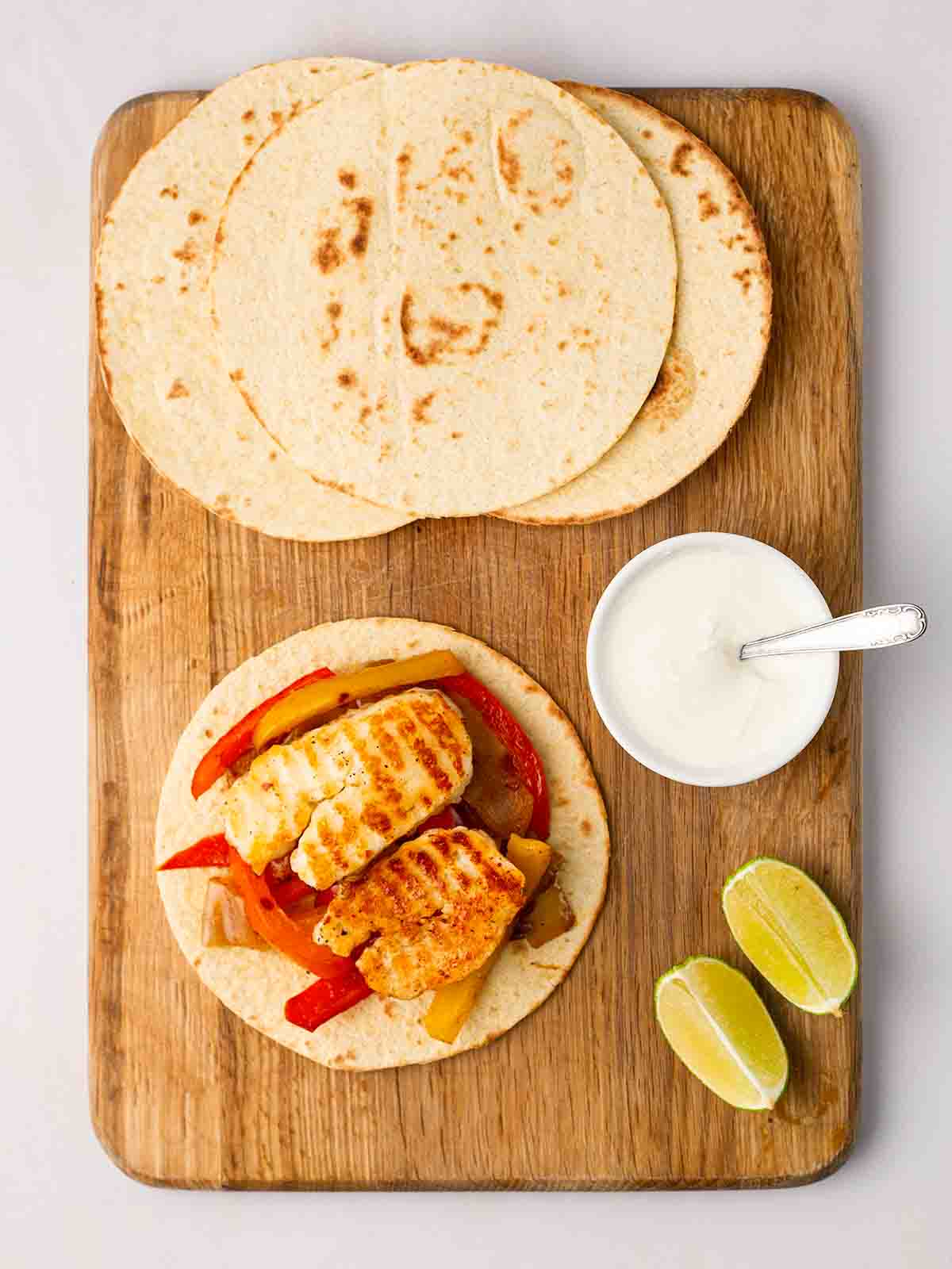 Wraps on a chopping with, one filled with halloumi fajitas and yoghurt dip to the side.