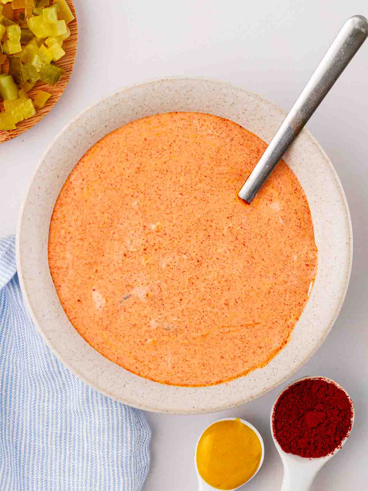 A bowl with a spoon, with an orange homemade Big Mac Sauce, with ingredients dotted around the edges.