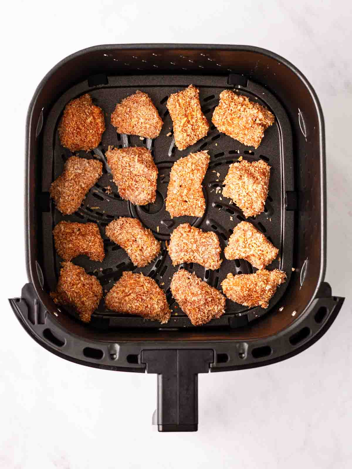 Pieces of uncooked chicken nuggets in an airfryer, ready to cook.