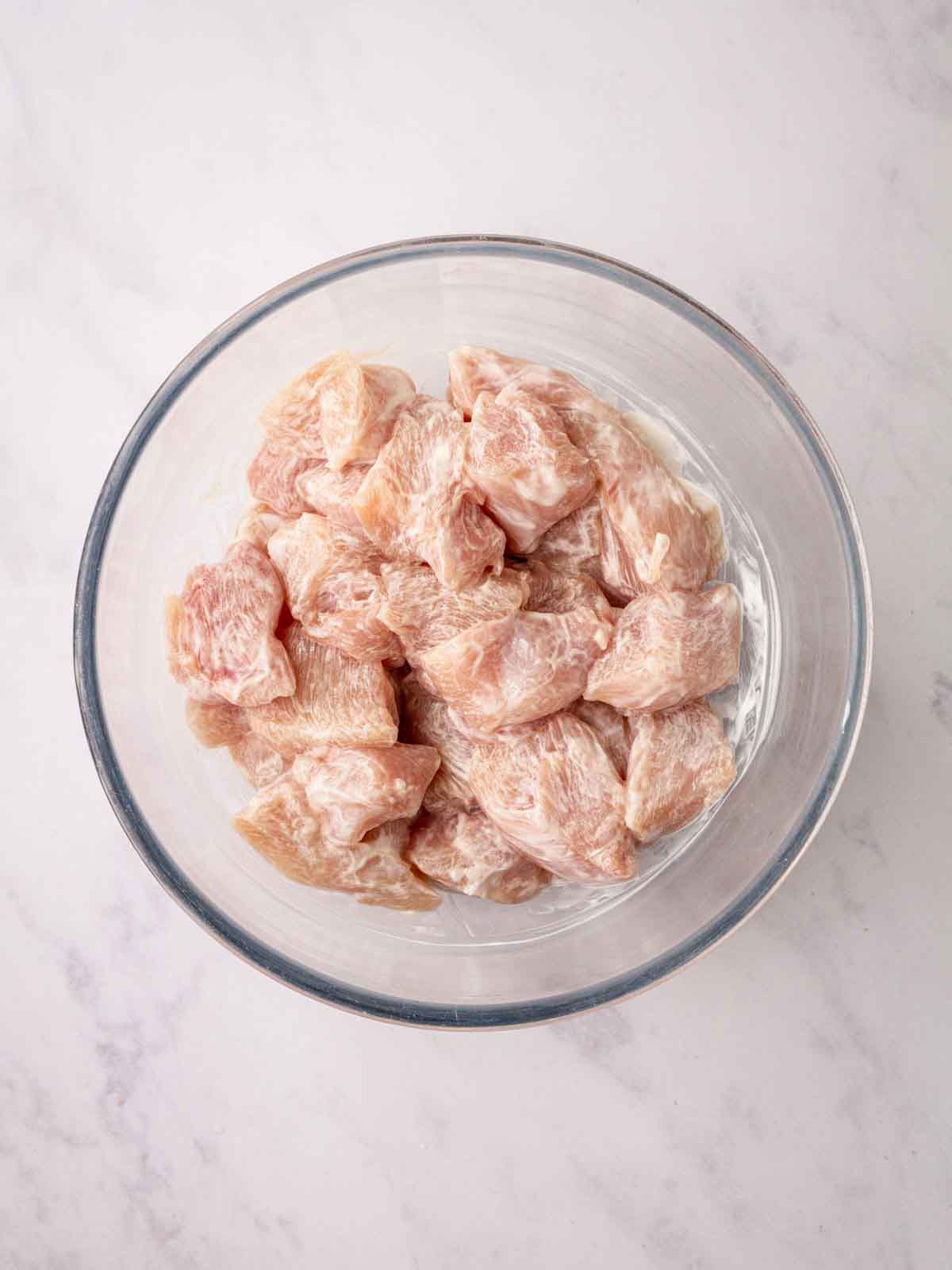 Raw chicken pieces coated in Greek yoghurt in a glass bowl for the recipe for Homemade Chicken Nuggets.