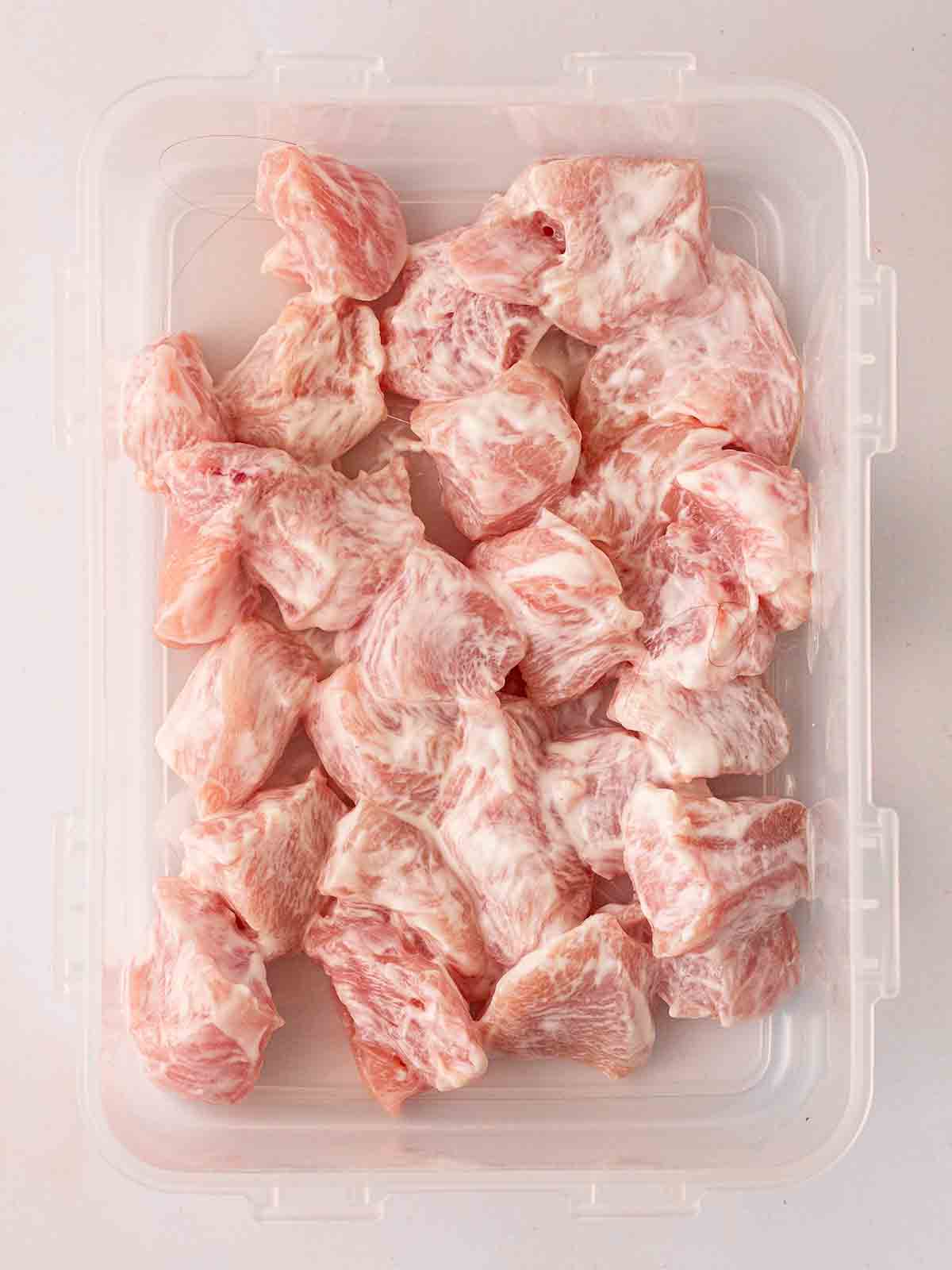 Pieces of raw chicken coated in Greek yoghurt in a Tupperware.