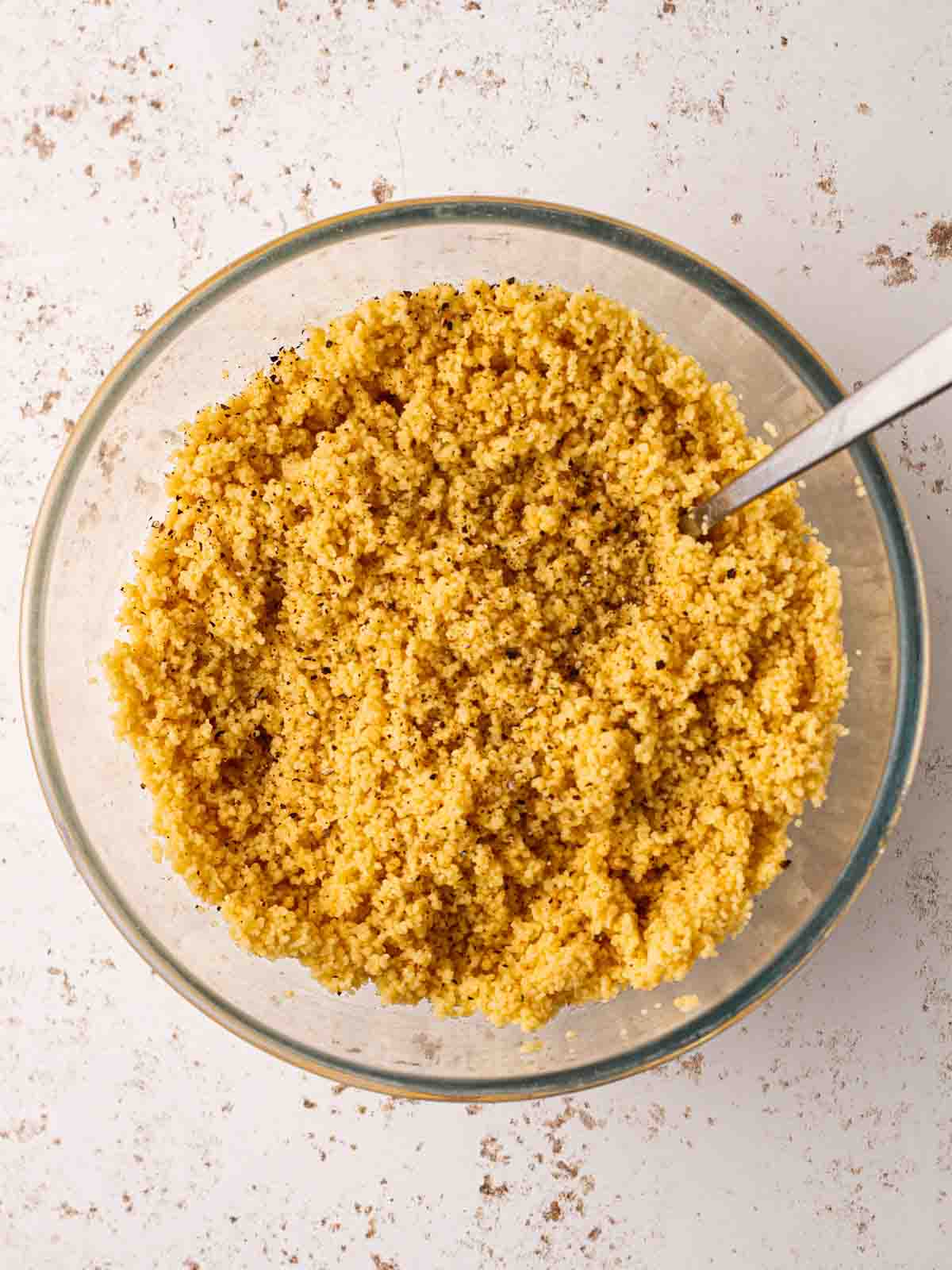 A glass bowl of fluffy couscous with a fork inside for step 2 in the recipe.