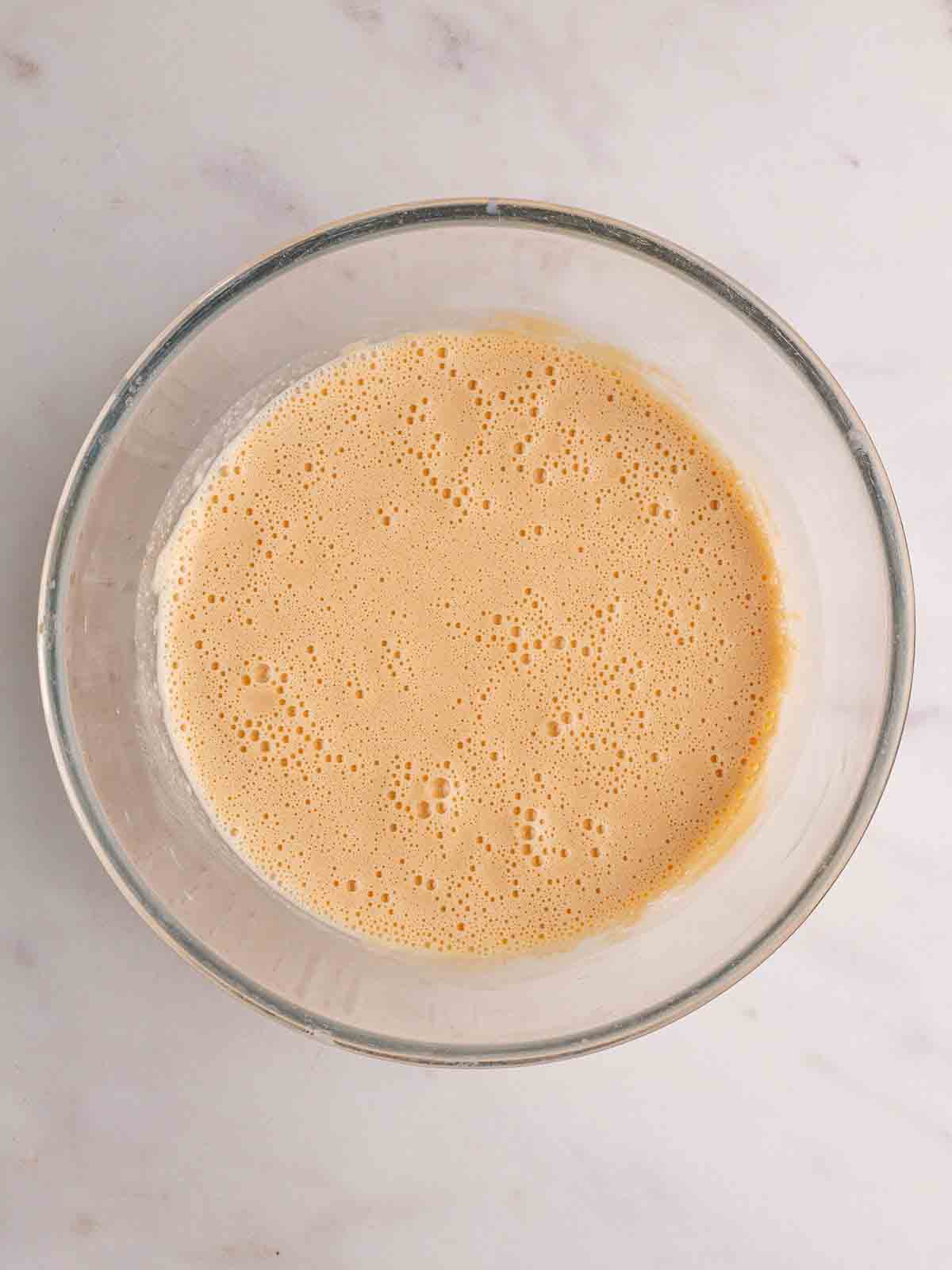 A yellow batter mixture in a glass bowl for step 2 in the recipe for Yorkshire Puddings.