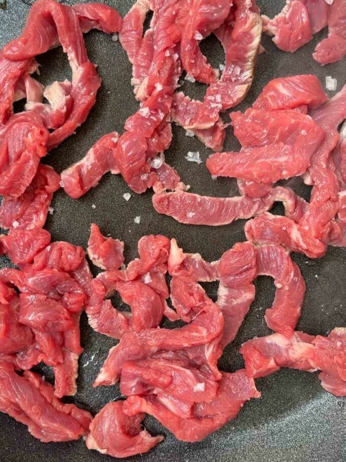 Strips of sirloin steak frying in a pan for step 1 in the recipe for Philly Cheesesteak.
