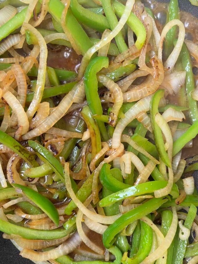Onions and peppers frying in a pan for step 2 in the recipe for Philly Cheesesteak.