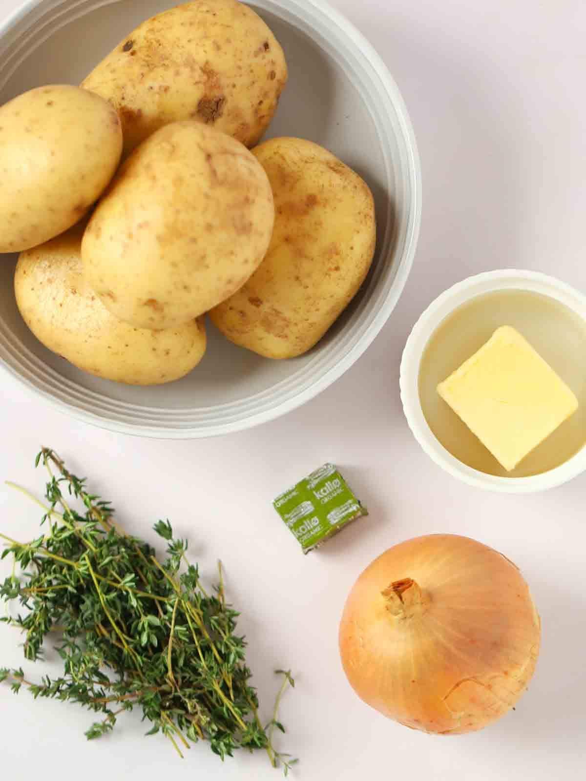 Ingredients for Boulangere Potatoes laid out on a white counter. The shot from above shows potatoes, butter, stock cube, onion and fresh thyme.