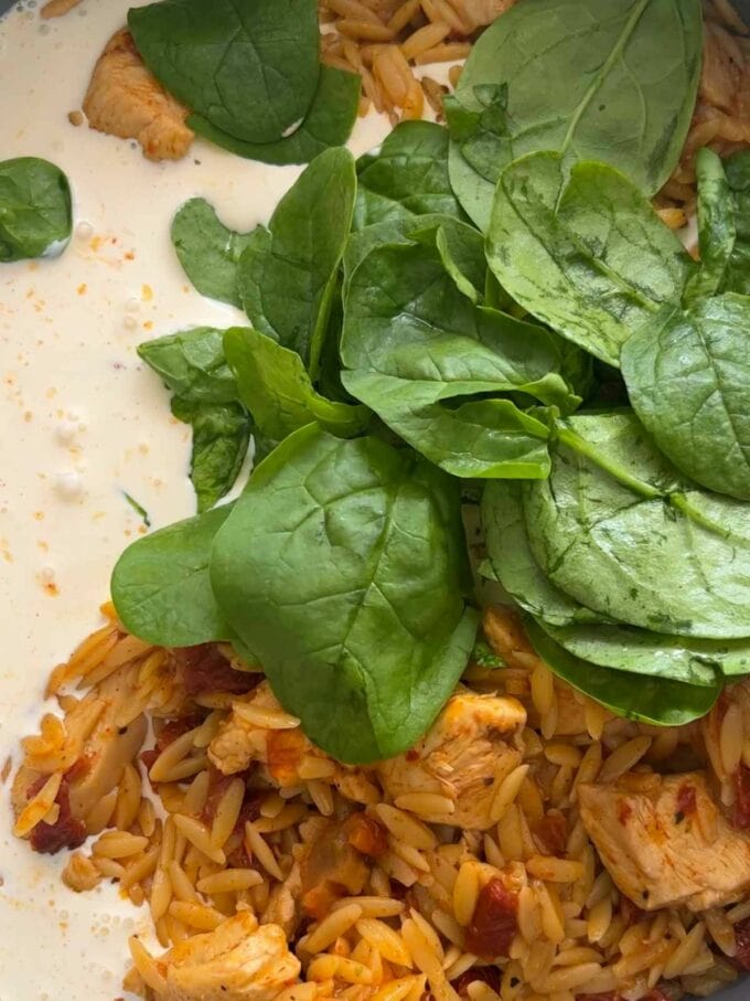 Spinach being adding to a pan with orzo, chicken and creamy for the recipe Marry Me Chicken Orzo, step 3.