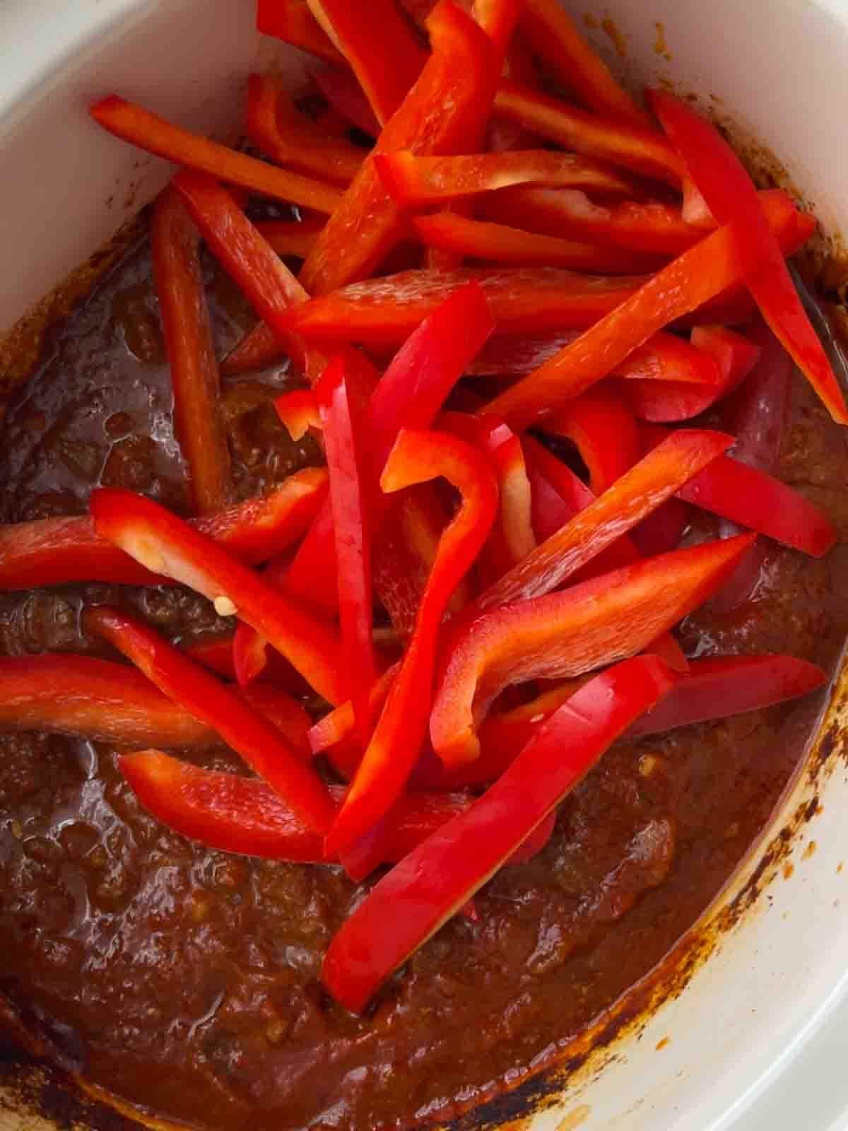 Red peppers going into a slow cooker beef goulash for step 2 in the recipe.