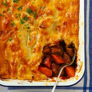 The corner of a puff pastry steak pie with a corner missing, with a spoon dipped in ready to serve a portion.