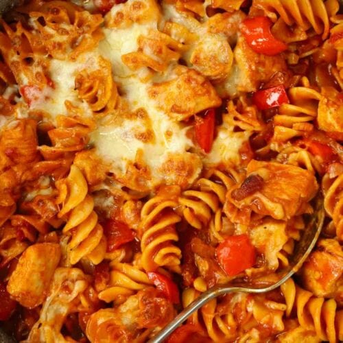 A spoon dipped in a pan of BBQ Chicken Pasta, ready to serve.