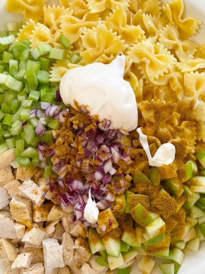 A bowl with the ingredients for chicken pasta salad, ready to be mixed together.