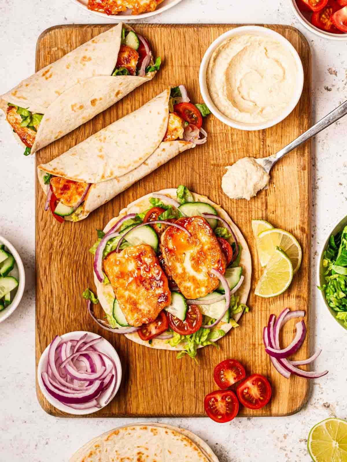 A board with halloumi wraps in progress, with two wraps made up, one open and salad around the edges.