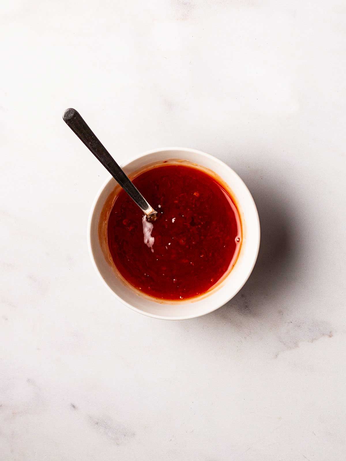 A small bowl of red sweet chilli dressing with a spoon sticking out of it for step 1 in the recipe for Halloumi Wraps.