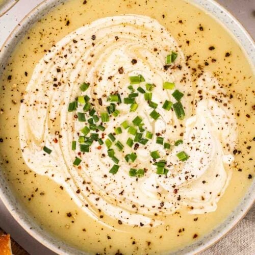 A close up of leek and potato soup with cream swirled on top with chives and black pepper.