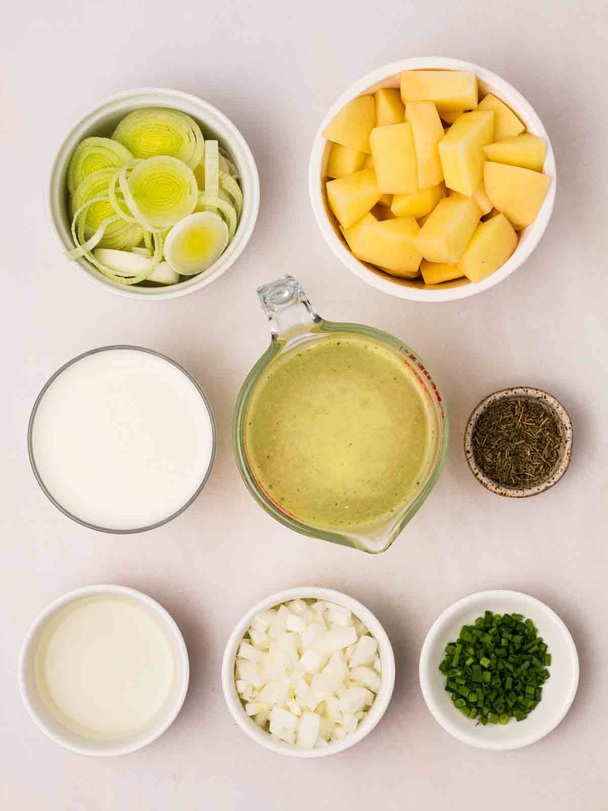 The raw ingredients for making leek and potato soup laid out in bowls on a white counter.