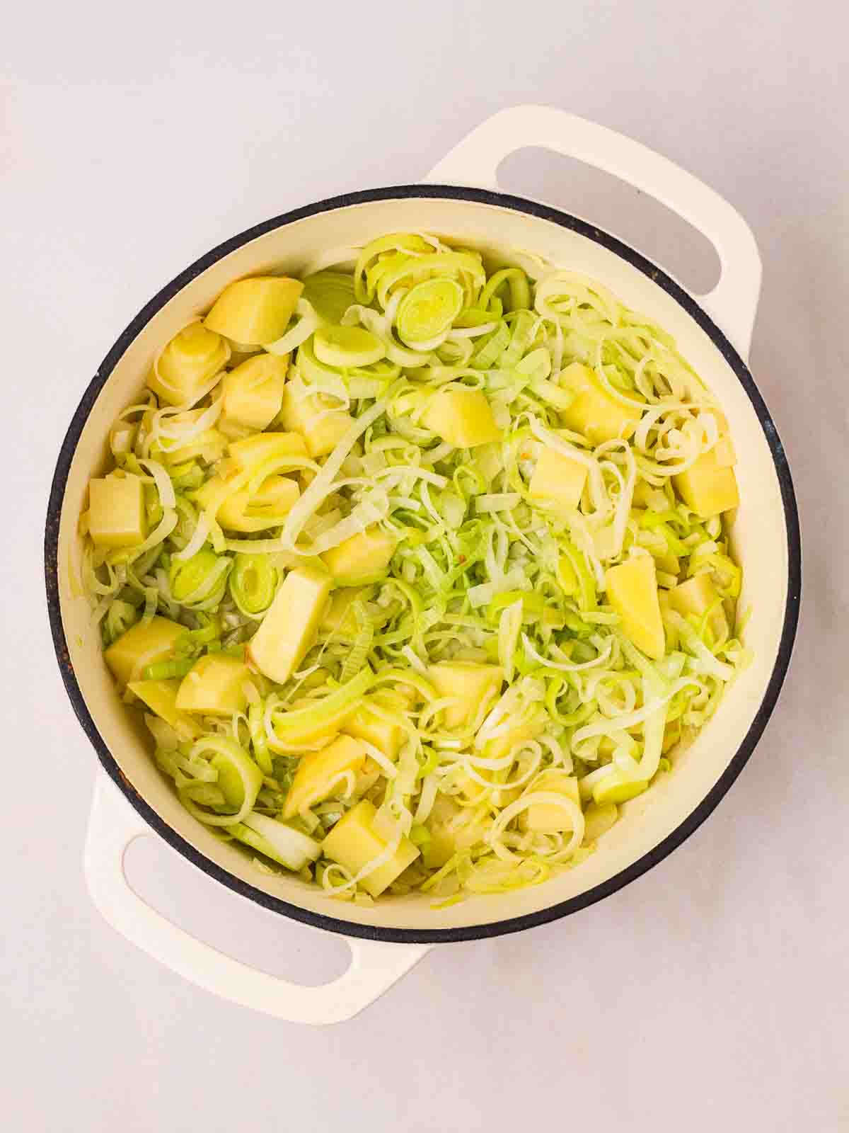 A large pan filled with sliced leeks and onion, and diced potato, for step 1 in the recipe for Leek and Potato Soup.
