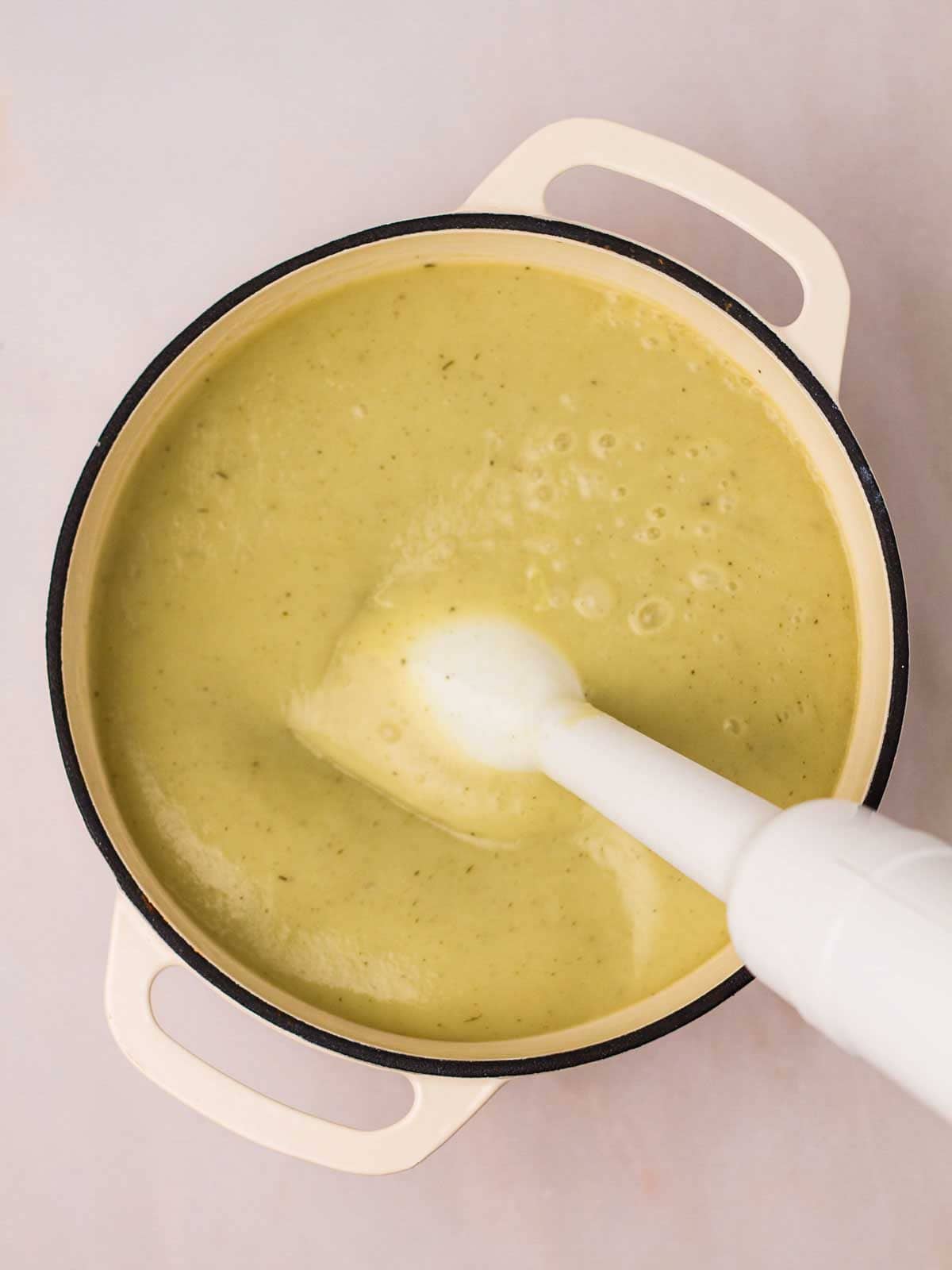 A large pan filled with blended Leek and Potato Soup, with a handheld blender inside for step 3 in the recipe.