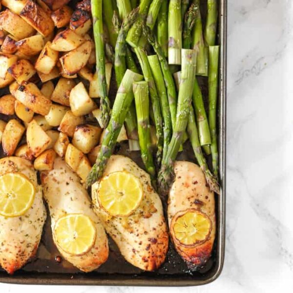A tray with baked lemon chicken and asparagus and potatoes, with lemon on top, ready to serve.