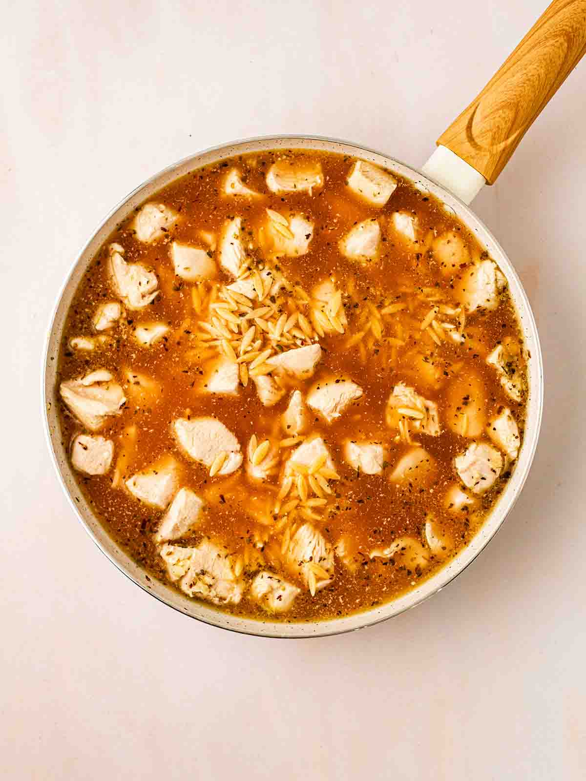 A pan filled with sauce, cooked chicken and raw orzo for step 2 in the recipe or Lemon Orzo Chicken.