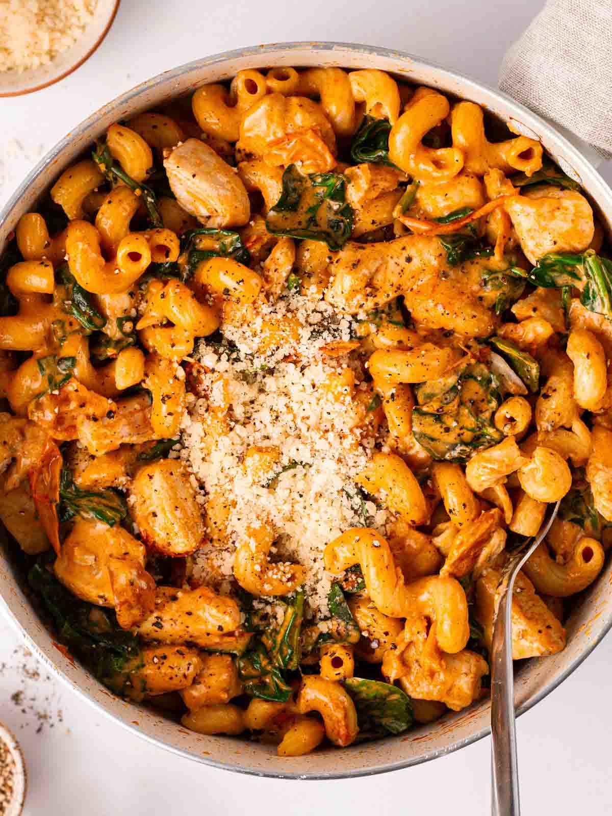 One pasta pasta on a table with cheese on top, ready to serve with a spoon straight out of the pan.