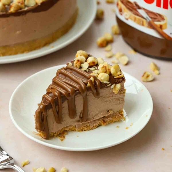 A slice of Nutella Cheesecake topped with chocolate and nuts on a white plate.
