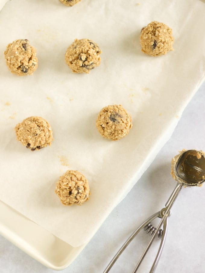Scoops of cookie dough on a baking sheet with ice cream scoop.