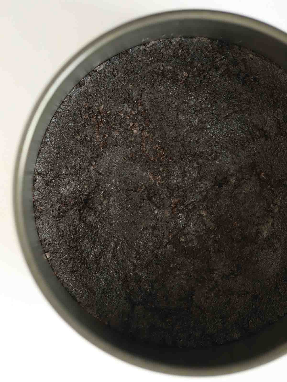 A dark biscuit base of crushed Oreo cookies in a tin for step 2 in the process for Oreo Cheesecake recipe.