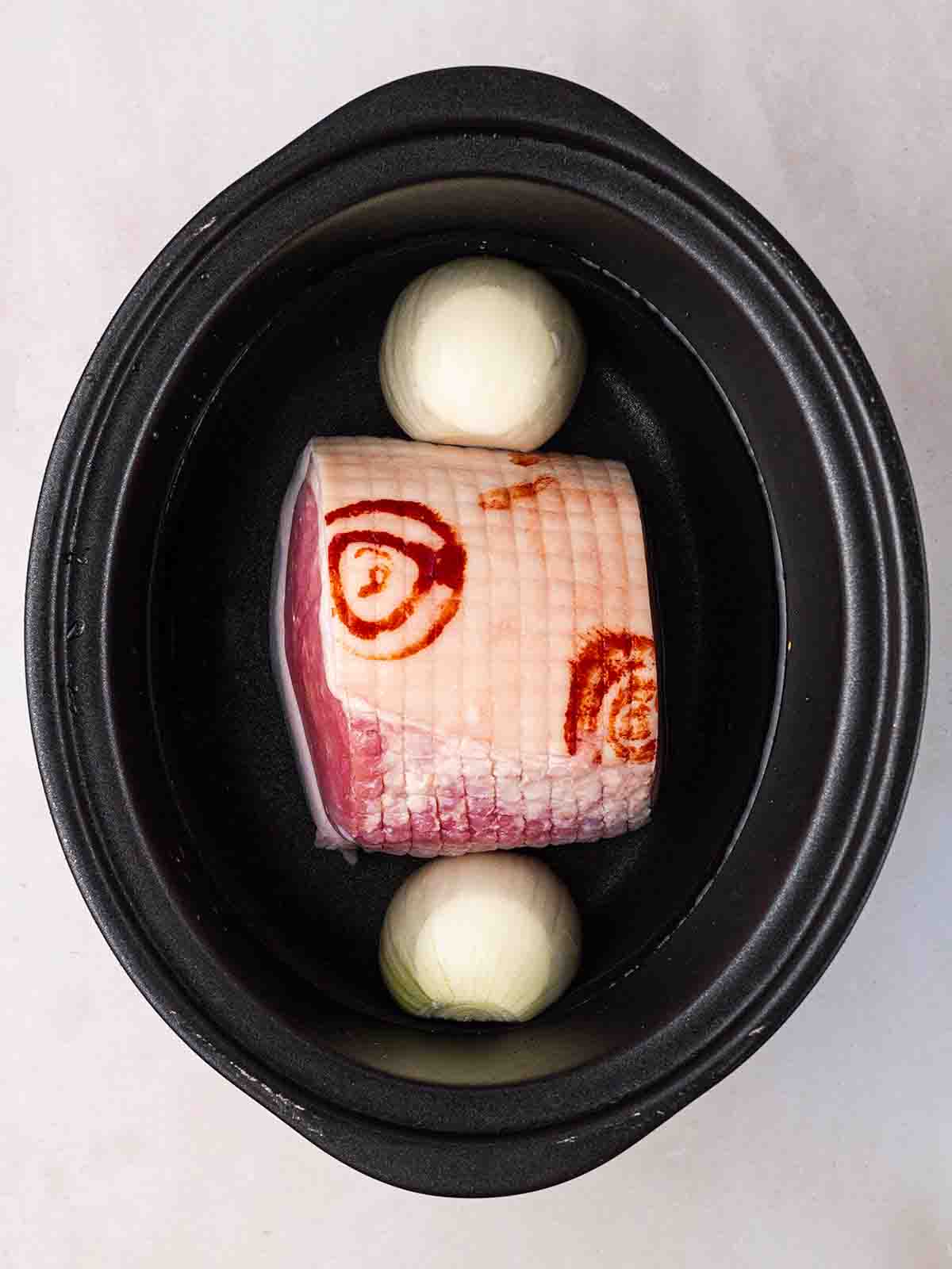 A slow cooker filled with a gammon joint, onion and water for step 1 in the recipe for Pea and Ham Soup.