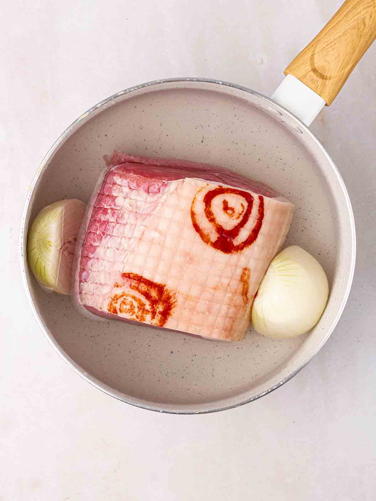 A raw gammon joint in a pan with onion for step 1 of the recipe Pea and Ham Soup, made on the stove.
