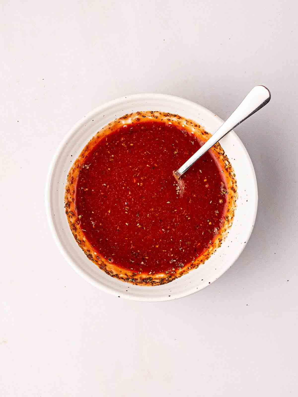 A round bowl with passata and herbs for step 1 in the recipe for Pizza Bagels.