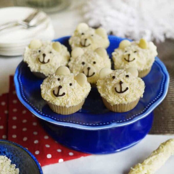 White chocolate cupcakes with a face decorate like a polar bear, on a blue cake stand.