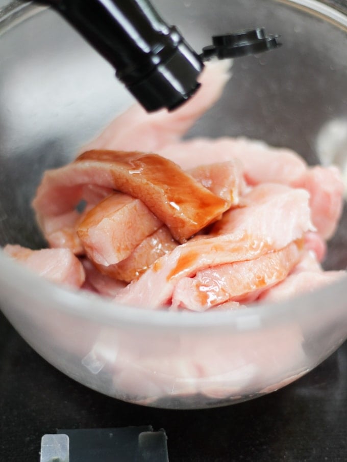 Strips of raw pork medallion with soy sauce on black work surface for pork stir fry recipe.