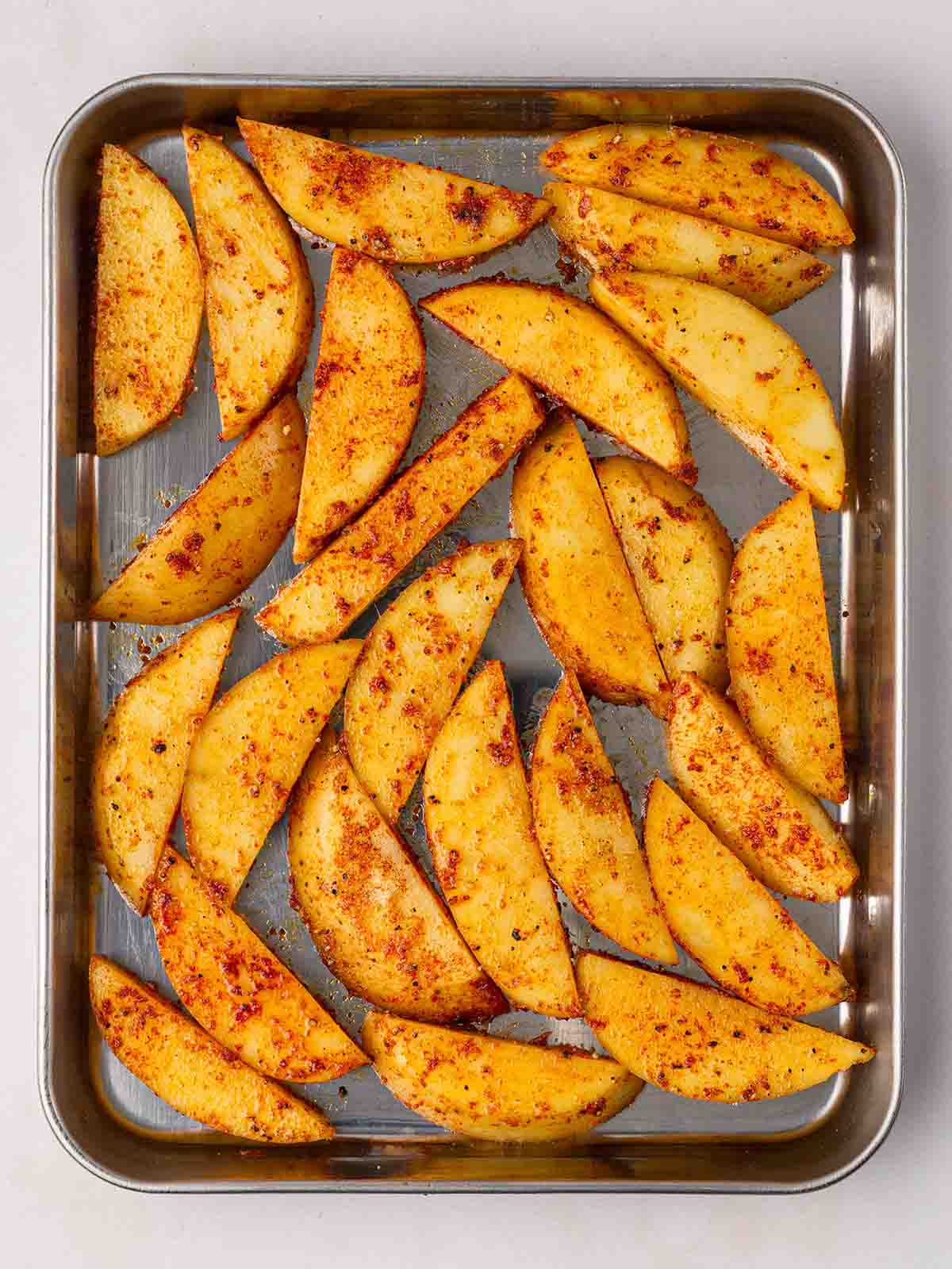 An oven tray filled with seasoned potato wedges.
