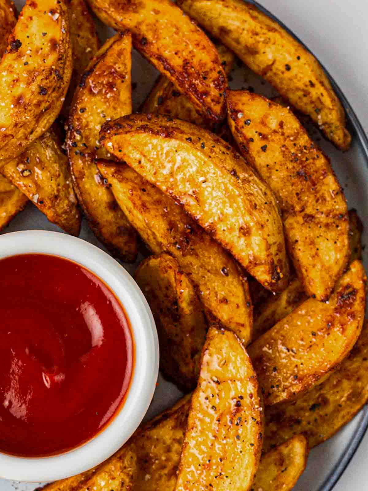 A close up of crispy homemade potato wedges with a small pot of ketchup.