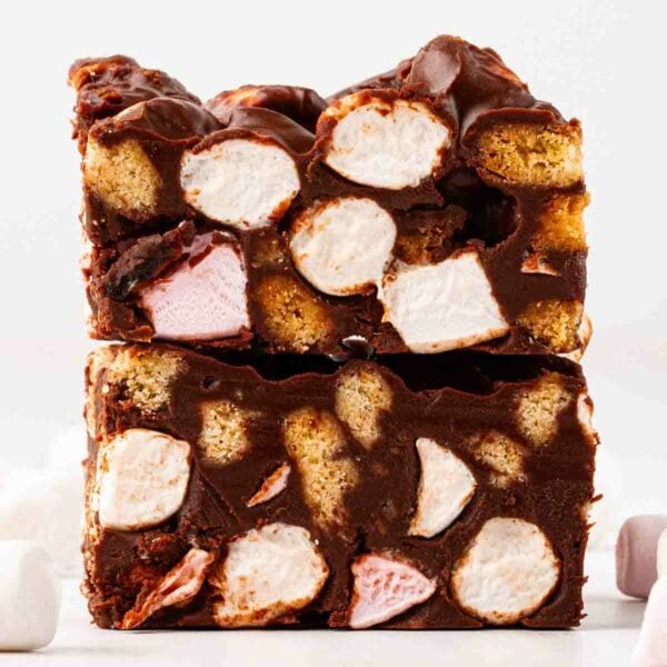 Two pieces of Rocky Road on top of each other, from the side, showing a filling of marshmallows and biscuits inside chocolate.