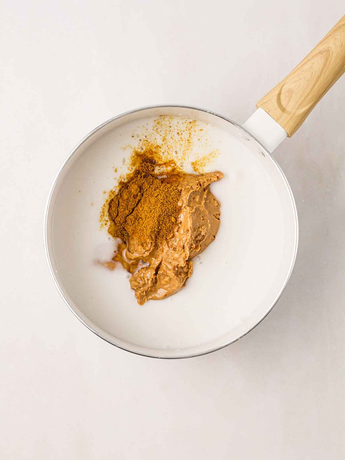 A pan filled with coconut milk, peanut sauce and curry powder for making homemade Satay Sauce.