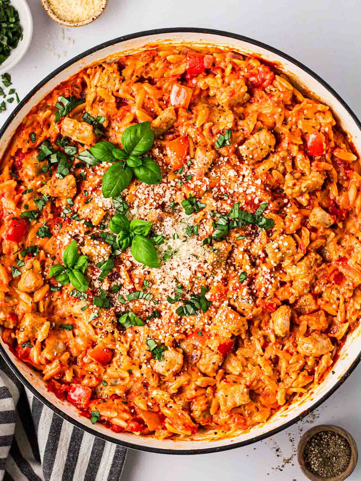A big white pan on a white counter filled with Sausage Orzo in a tomatoey sauce and basil on top.