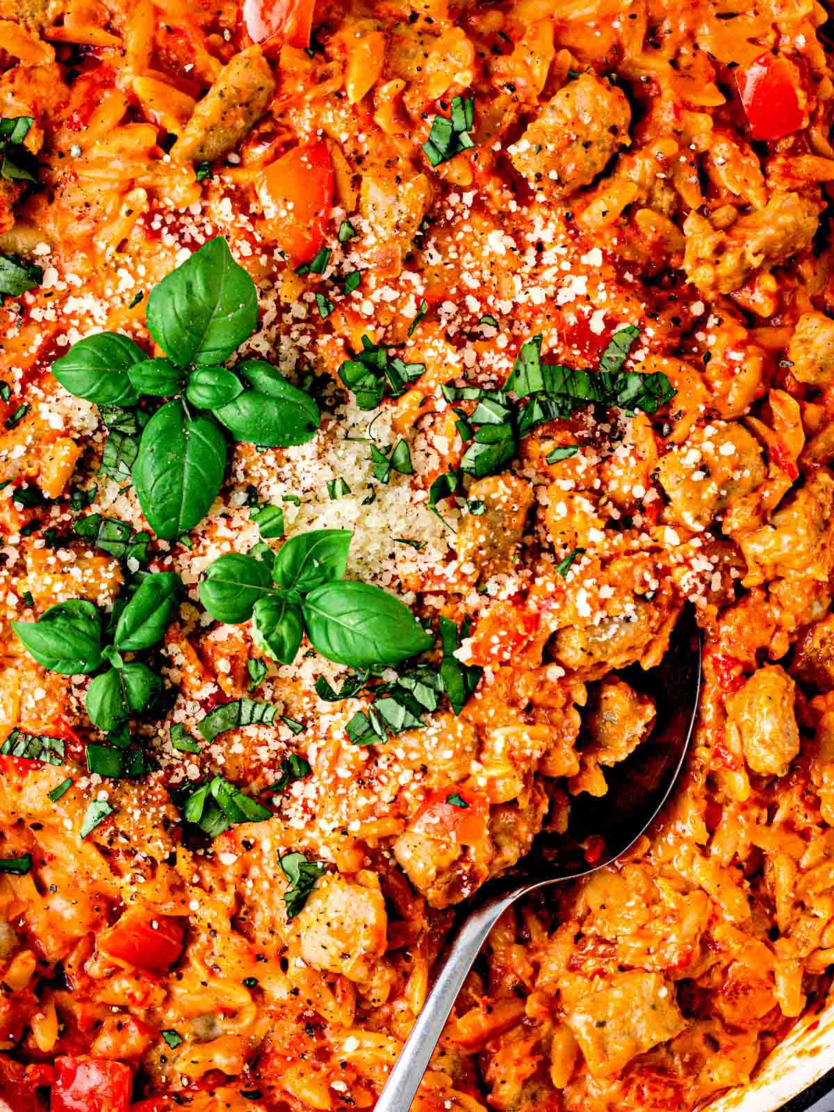 A close up of Sausage Orzo pasta with a spoon and basil on top.