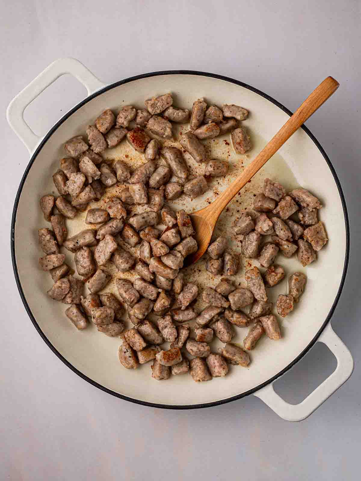 A pan filled with chunks of sausage, browning in oil, for step 1 in the recipe for Sausage Orzo.
