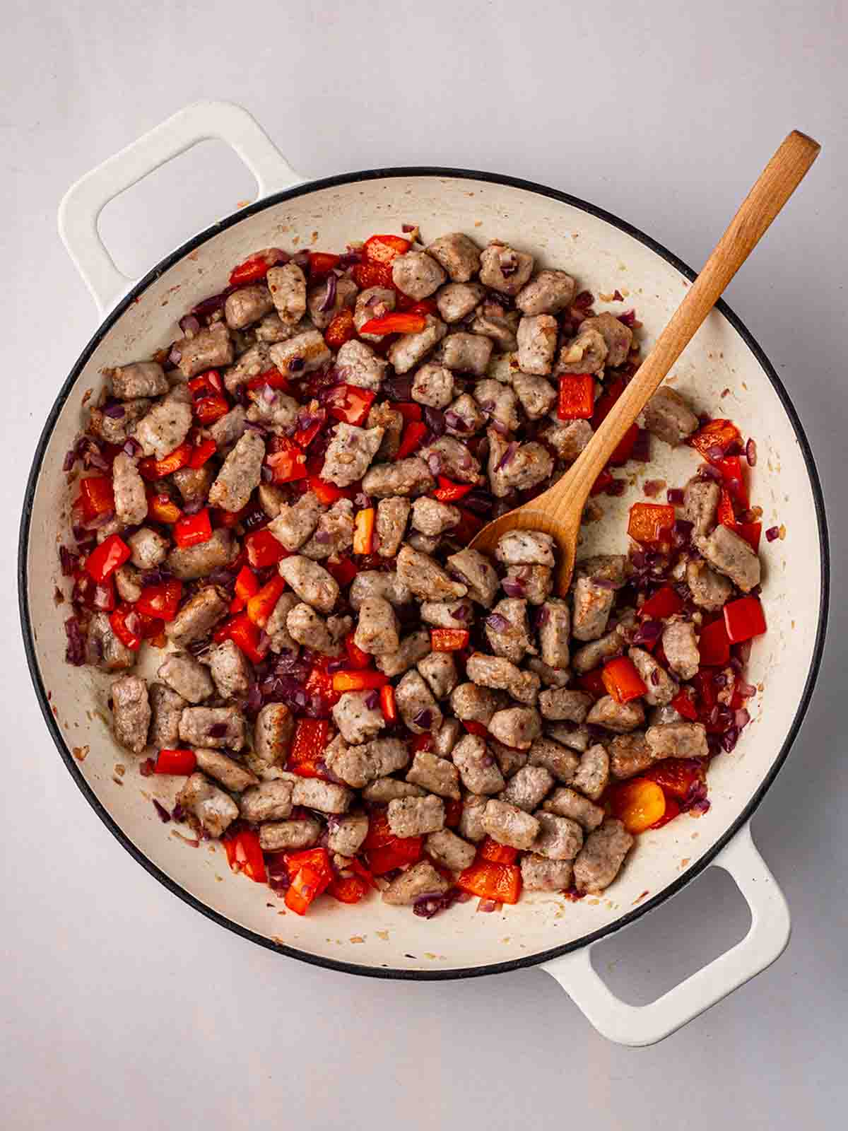 Chucks of cooked sausage with red pepper cooking in a pan for for step 2 in the recipe for Sausage Orzo.