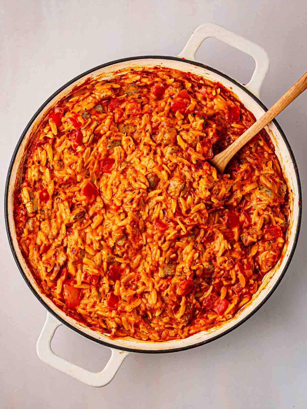 A spoon stirring a white pan filled with Sausage Orzo for for step 4 in the recipe for Sausage Orzo.
