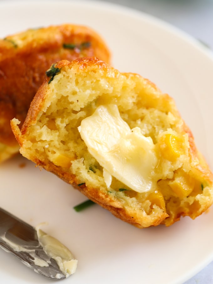A cheese savoury muffin on a plate in half, with butter melting into it.