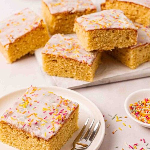 A square of School cake on a plate with a cake fork, with other pieces of cake in the background.