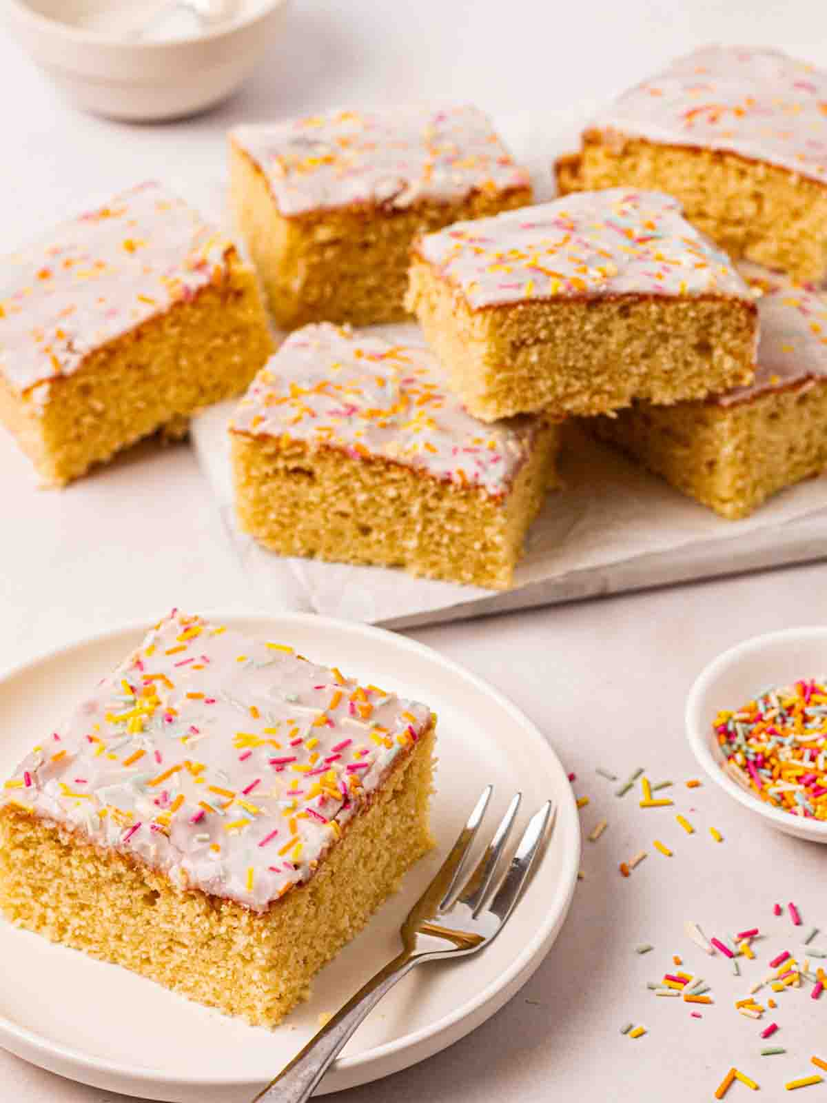A square of School cake on a plate with a cake fork, with other pieces of cake in the background.