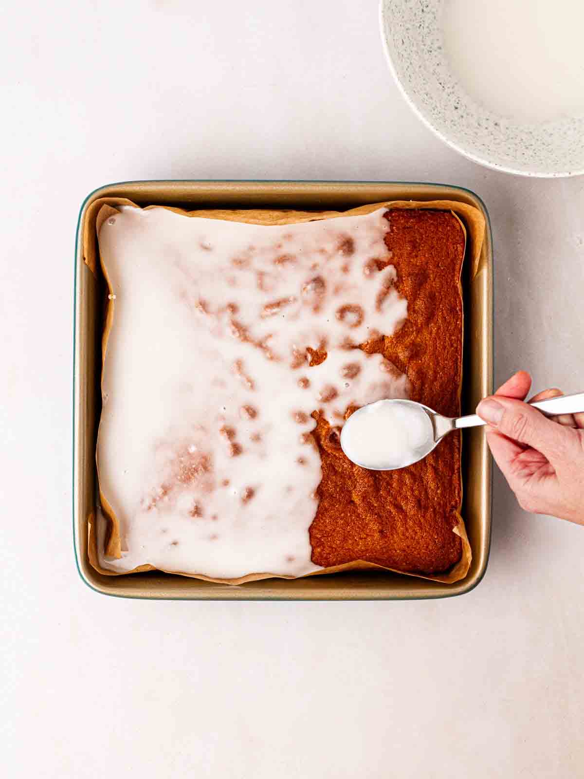White icing being poured over a sponge cake for a School Cake recipe.