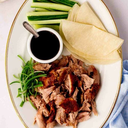 A platter with cooked slow cooker duck shredded, Chinese pancakes, cucumber, spring onion and sauce.